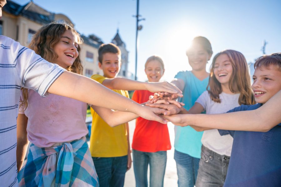 Group of happy teenagers standing in a circle with their hands joined in the middle